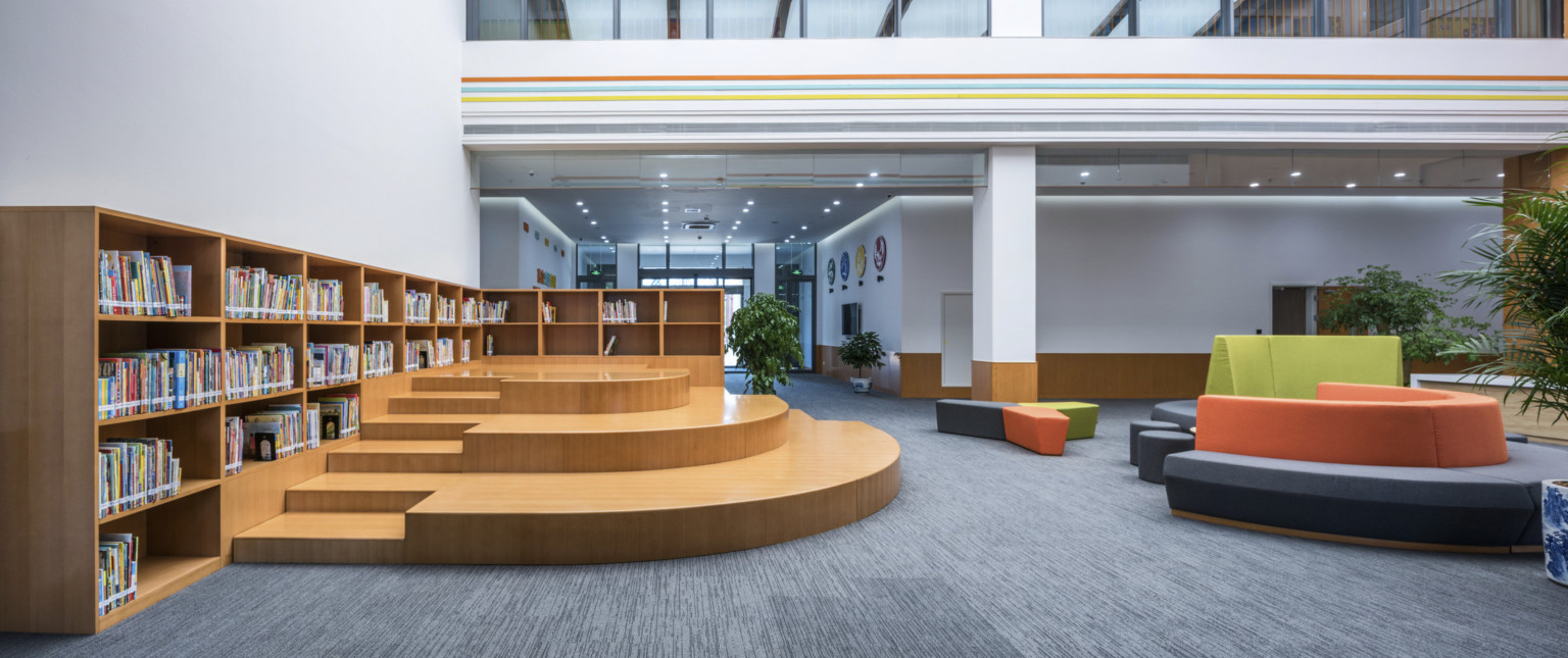 Another view of the atrium with seating to the right. Left, a wood L shaped bookcase lines the wall with stepped seating