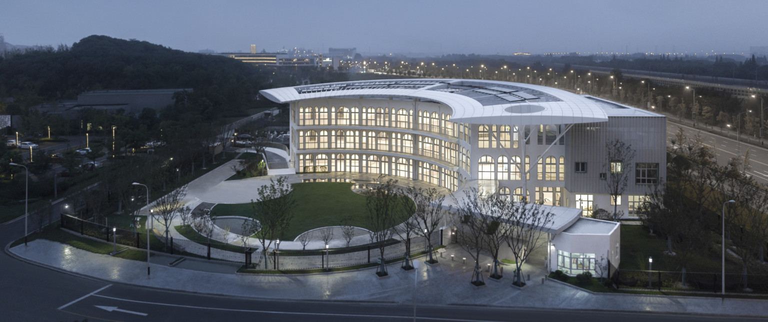 Round lawn in front of semi circular facade of school with covered driveway to right. Arched windows line front and side