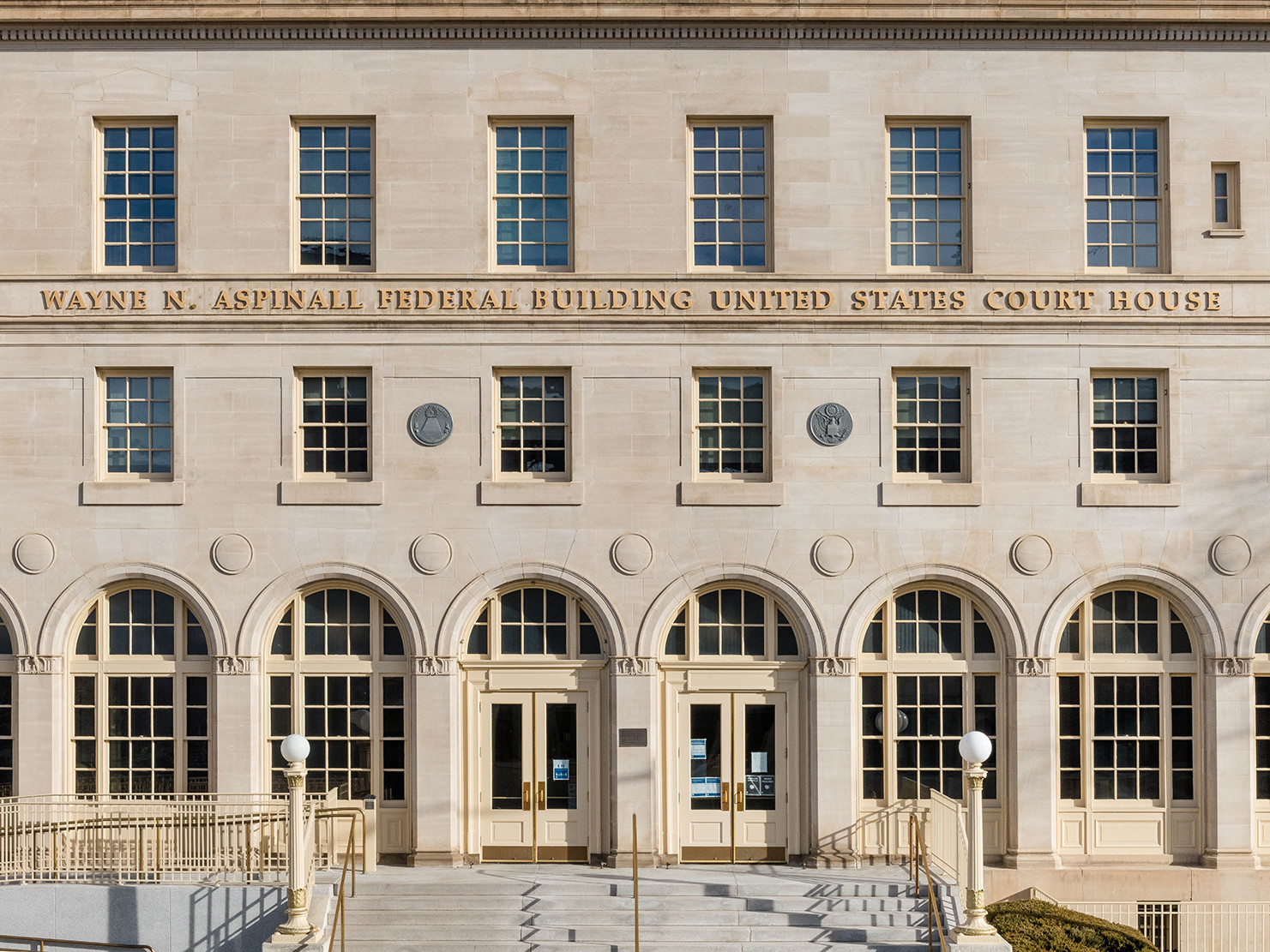 tan stone italianate renaissance facade with arched ground level windows and doors. letters between two rows of square windows