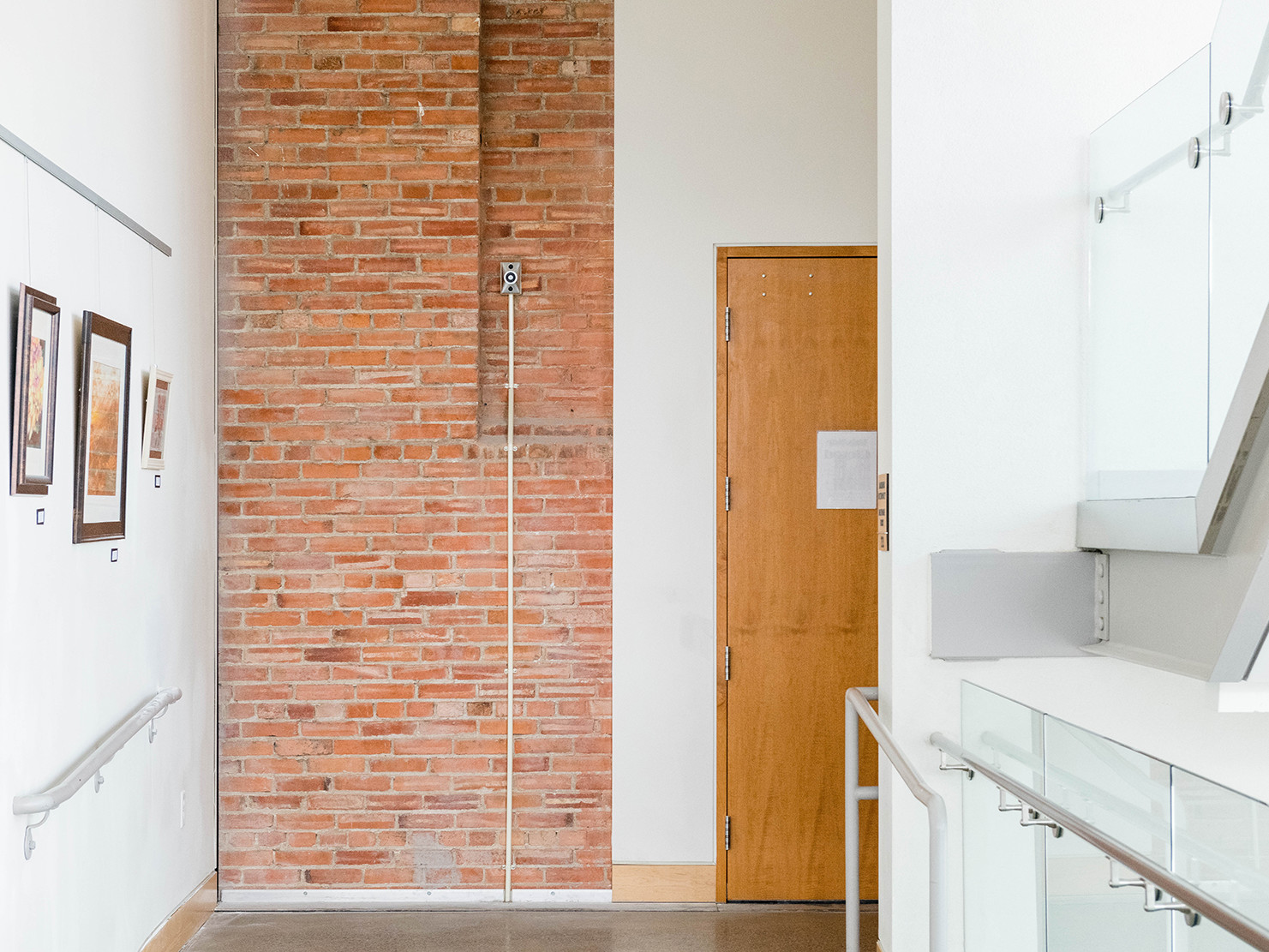 white gallery walls with framed photos hanging, exposed brick wall with polished concrete floor, and a glass and steel stair