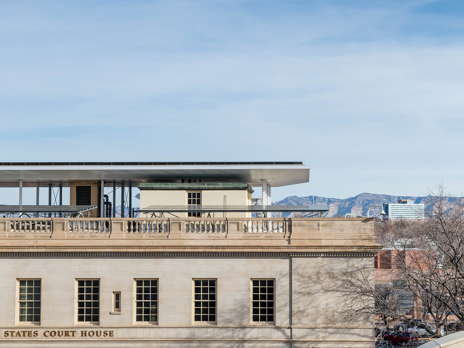 tan stone building with parapet and balustrade and rooftop mounted photovoltaic solar canopy. rocky mountains in the distance