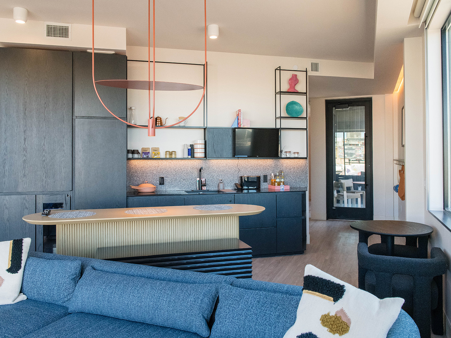 blue low back sofa and natural wood kitchen island beneath contemporary pink chandelier. kitchen sink in black cabinets