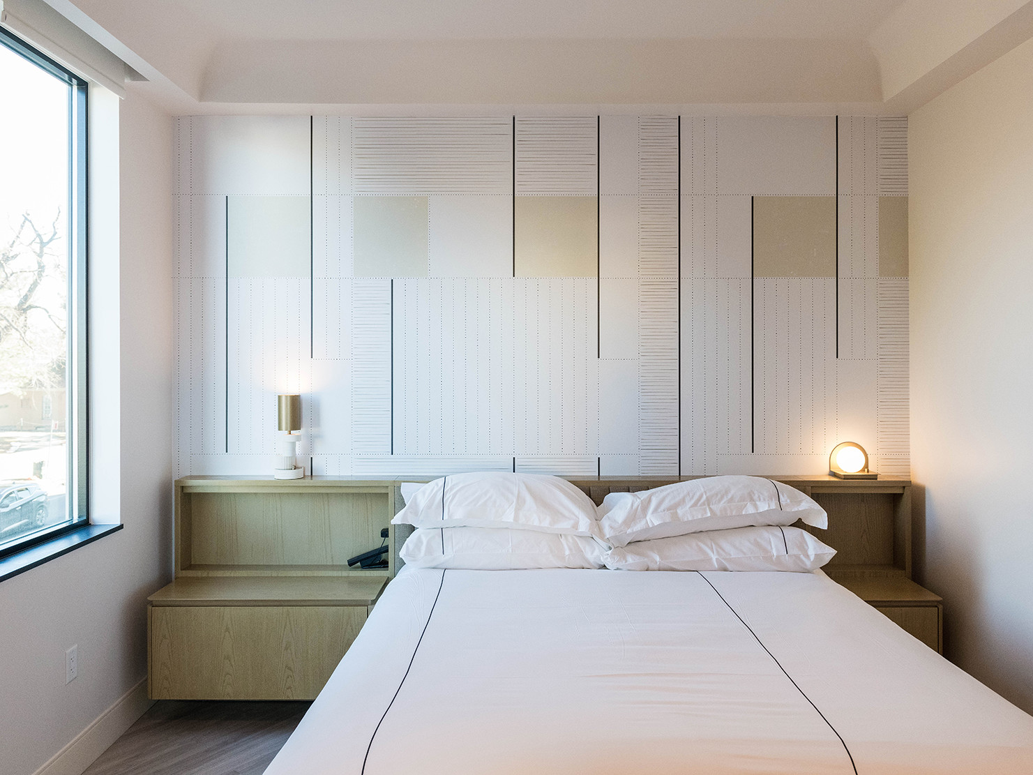 a wall with neutral color and geometric patterns behind a low profile headboard and side tables. white linens on the bed.