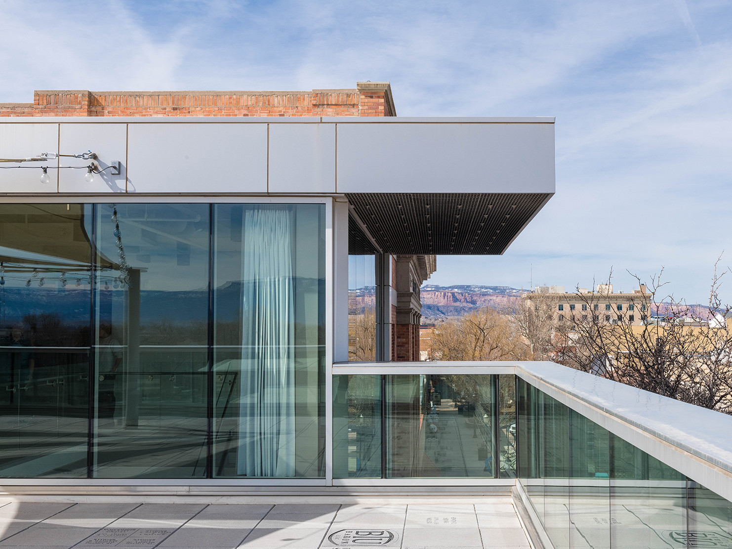Glass and steel rooftop deck with a glass balustrade and steel cap. Views of adjacent brick building and the Rocky Mountains