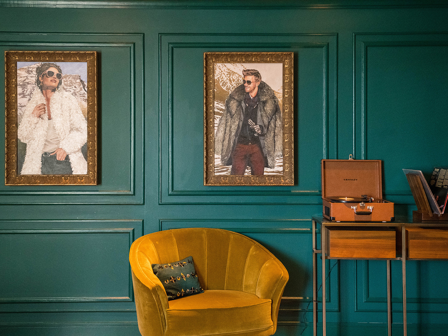 deep green walls with molding and gold filigree portrait frames. gold velvet lounge chair and wood table with vinyl records