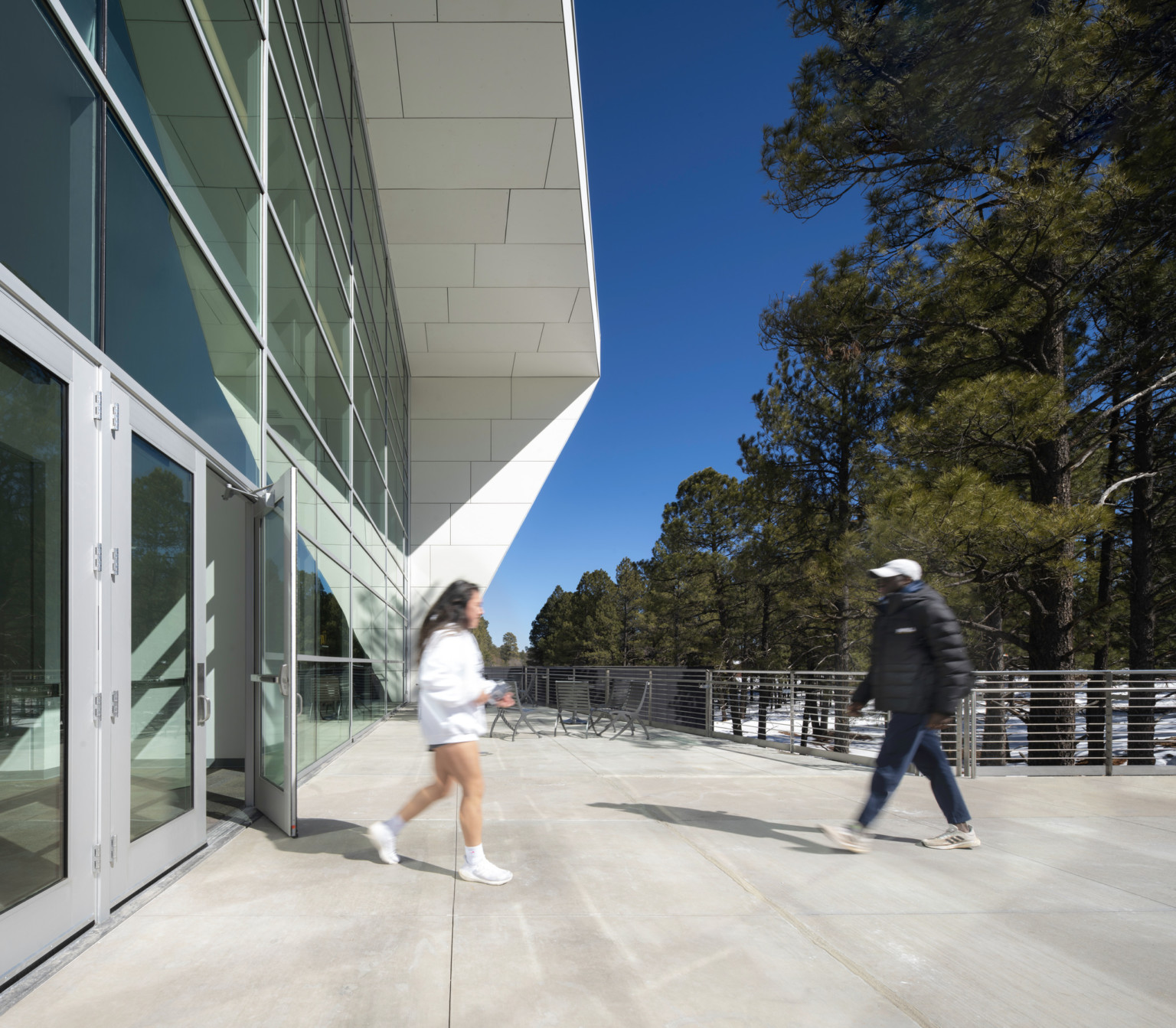 angular white paneled exterior canopy over glass facade with glass doors leading onto concrete plaza lined with wire railing