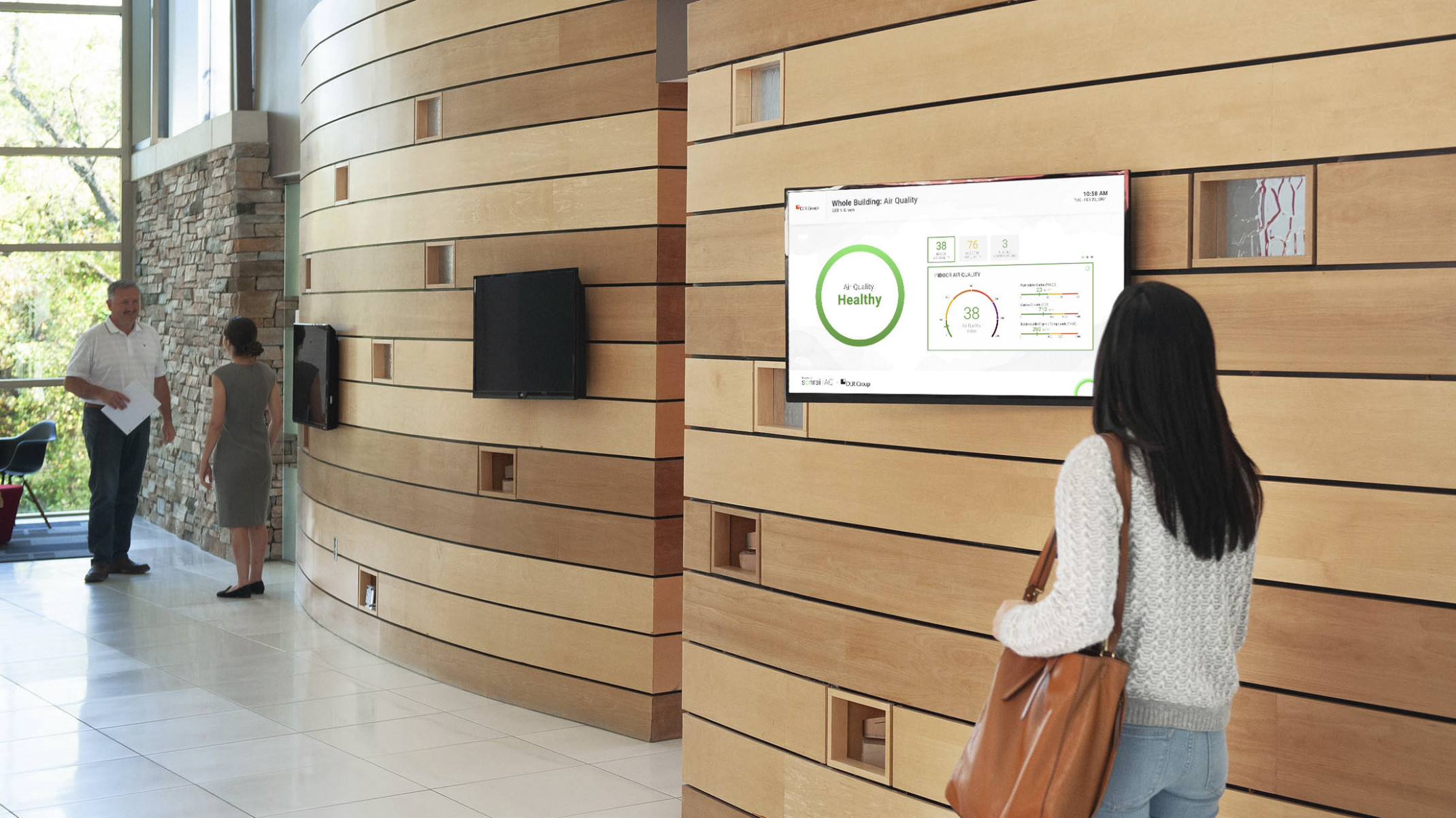 person in office building looking at tv screen on wood panel lobby wall displaying current air quality data on it