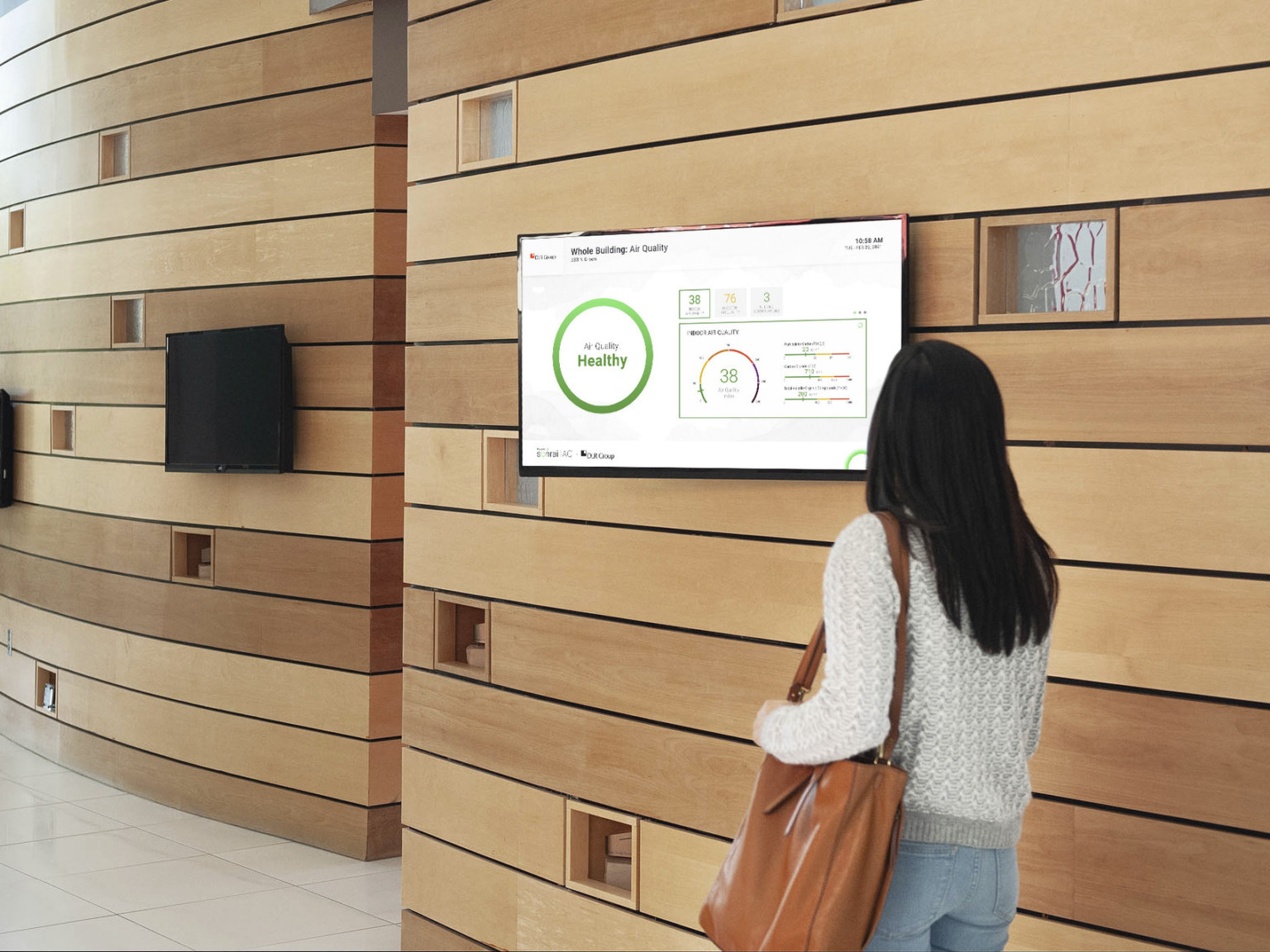 person in office building looking at tv screen on wood panel lobby wall displaying current air quality data on it