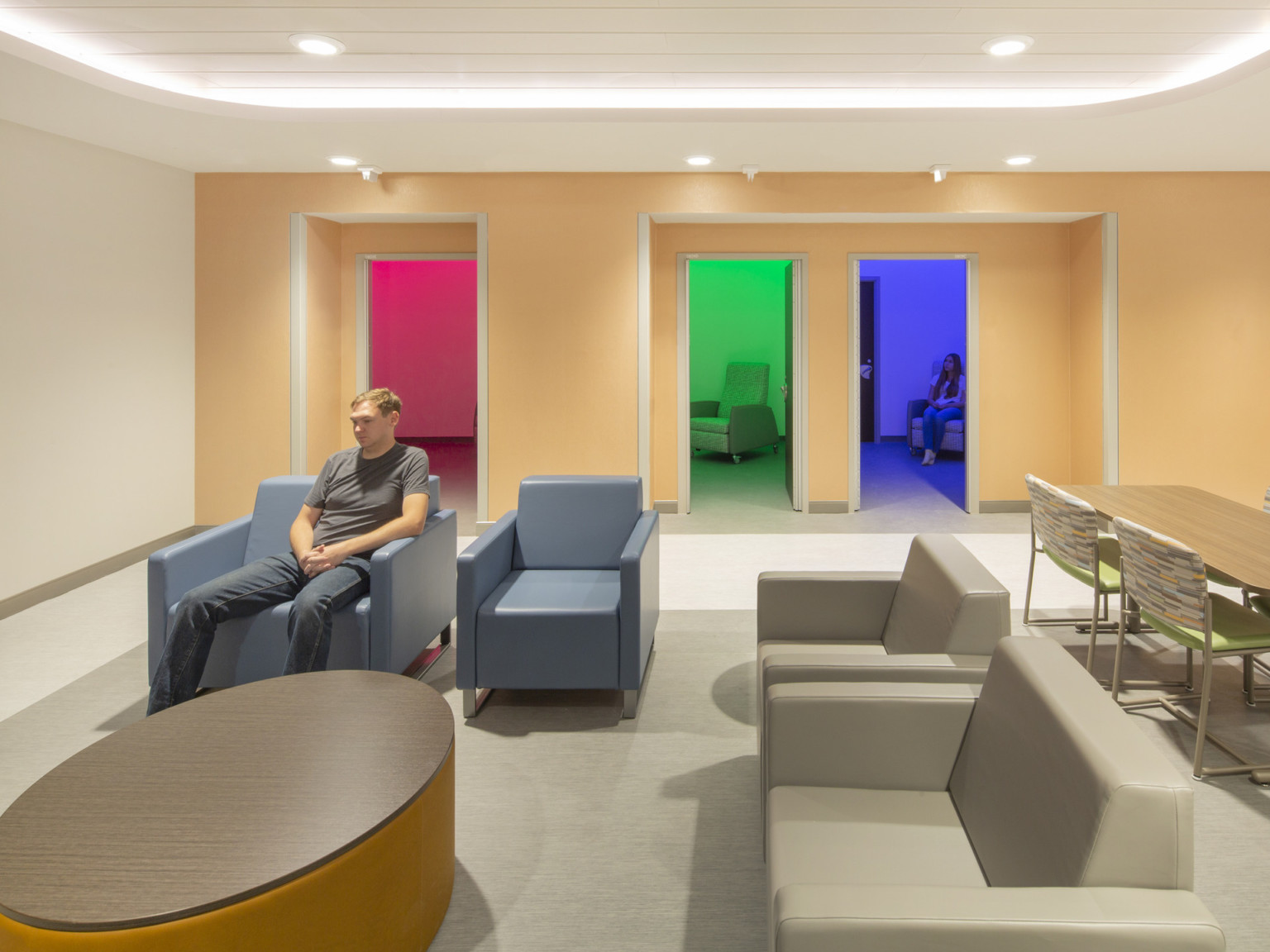 Seating area in front of small recessed rooms with red, green, or blue light. Arm chairs in each room and outside
