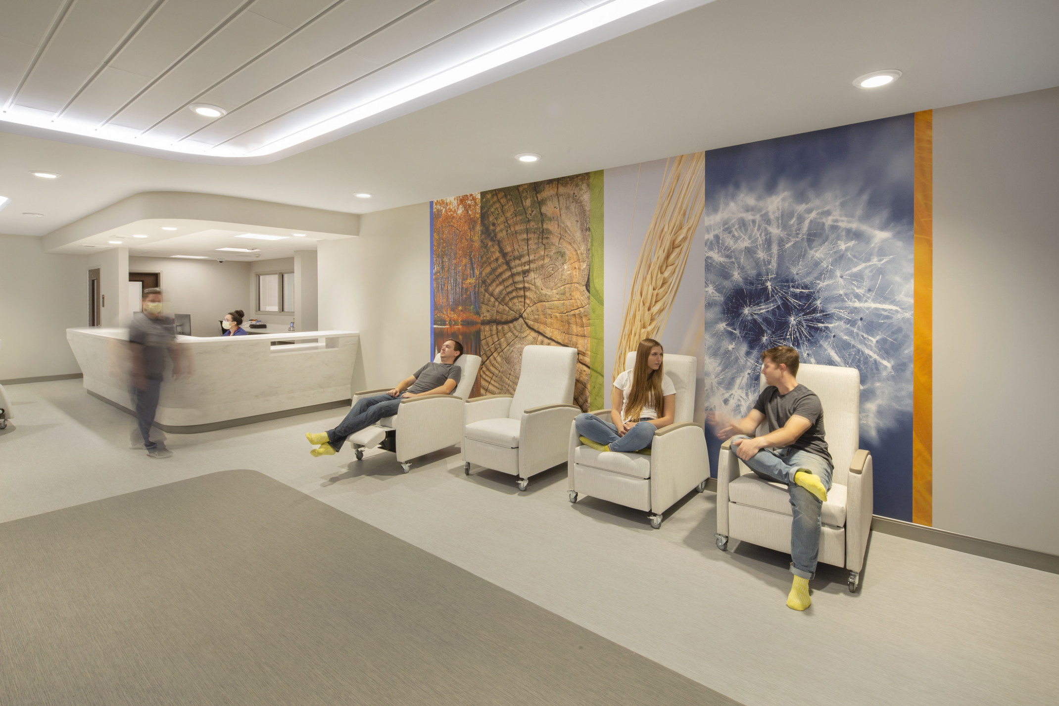 Nebraska Medicine Psychiatric Emergency Services Unit interior hallway. 3 people sit in recliners in front of photo mural