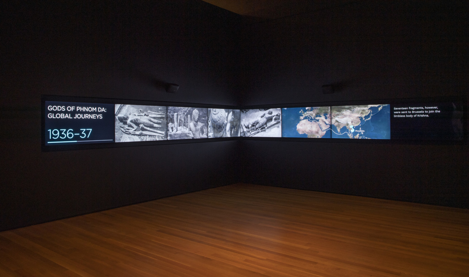 wood floor and two black walls with a timeline on large digital screens showing the journeys of the gods of phnom da 1936-37