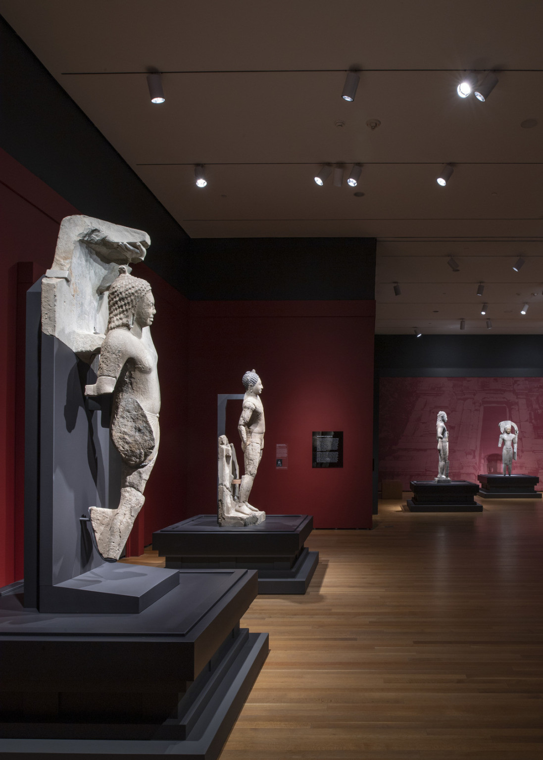white sculpture remnants mounted on black supports on black plinths in a gallery room with maroon walls and wood floors