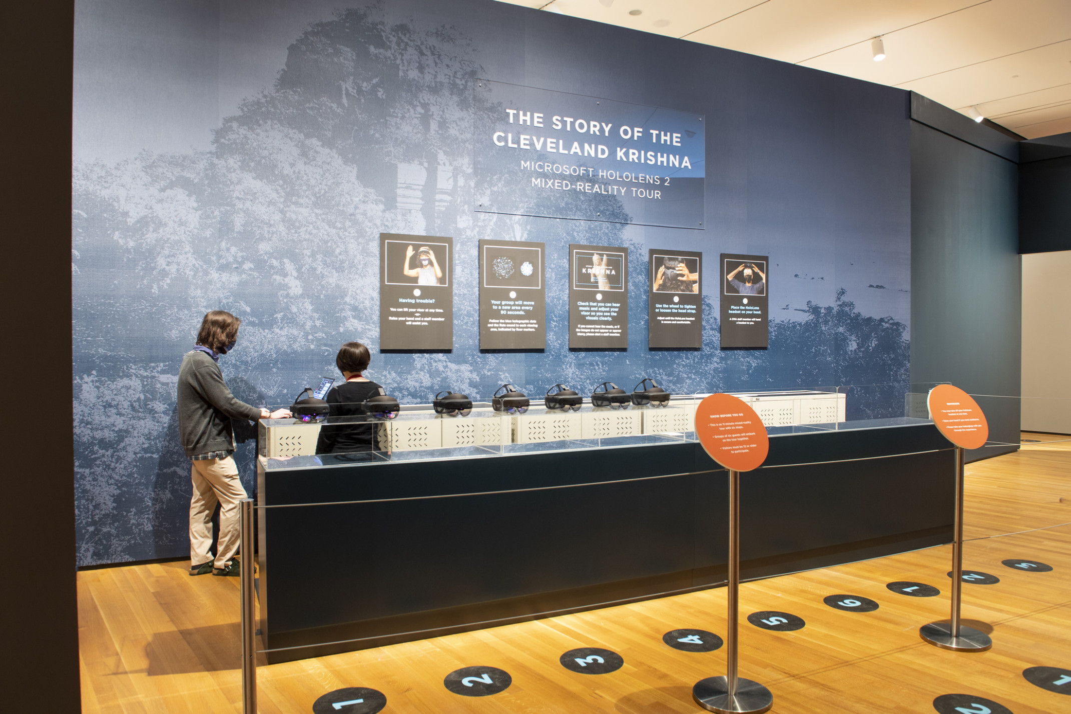 blue tinted wall graphic of cambodian forest with glass display case in the foreground with queueing ropes and tour signs