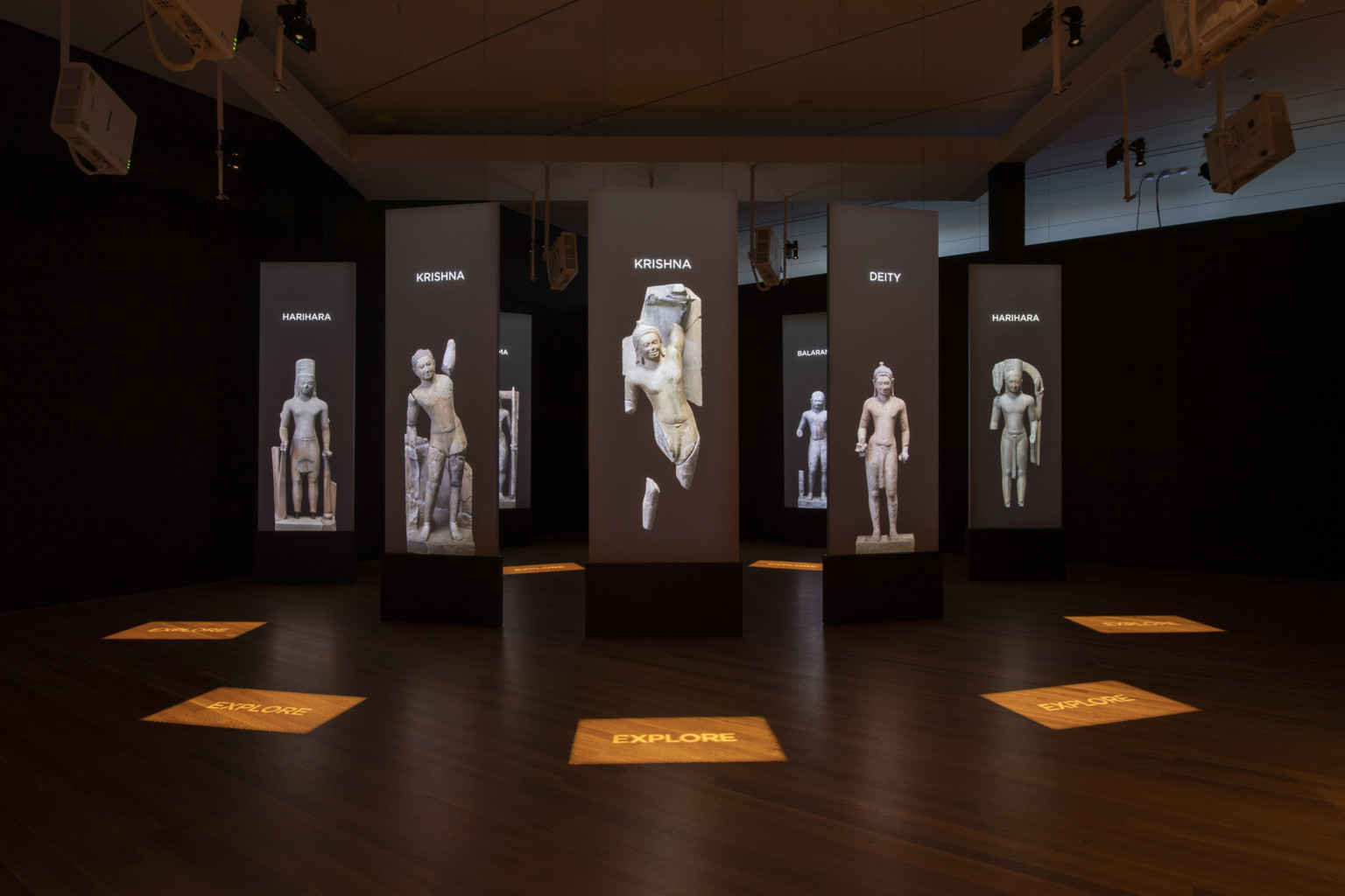 a darkened room with screens and stone statue images suspended in a circle pattern with illuminated signage on the wood floor