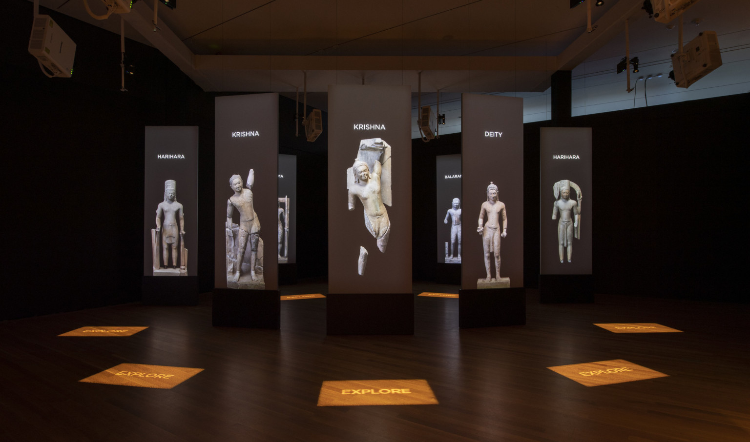 a darkened room with screens and stone statue images suspended in a circle pattern with illuminated signage on the wood floor