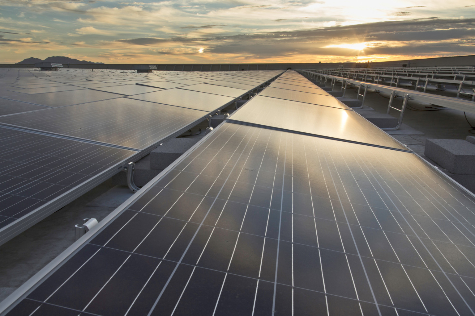 a long stretch of reflective black photovoltaic panels stretching into the horizon line of a sunset on a rooftop skyline