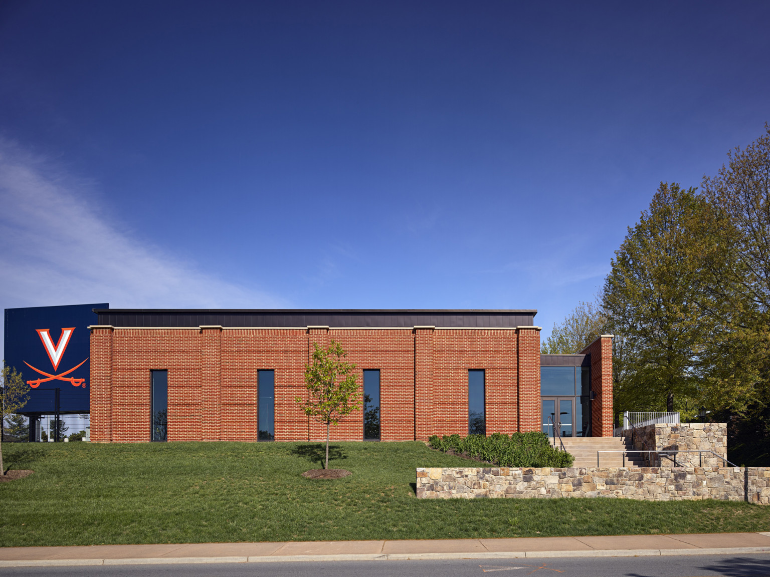 Double height brick building with glass walled entry to right at the top of stairs. Virginia Cavaliers logo on screen, left