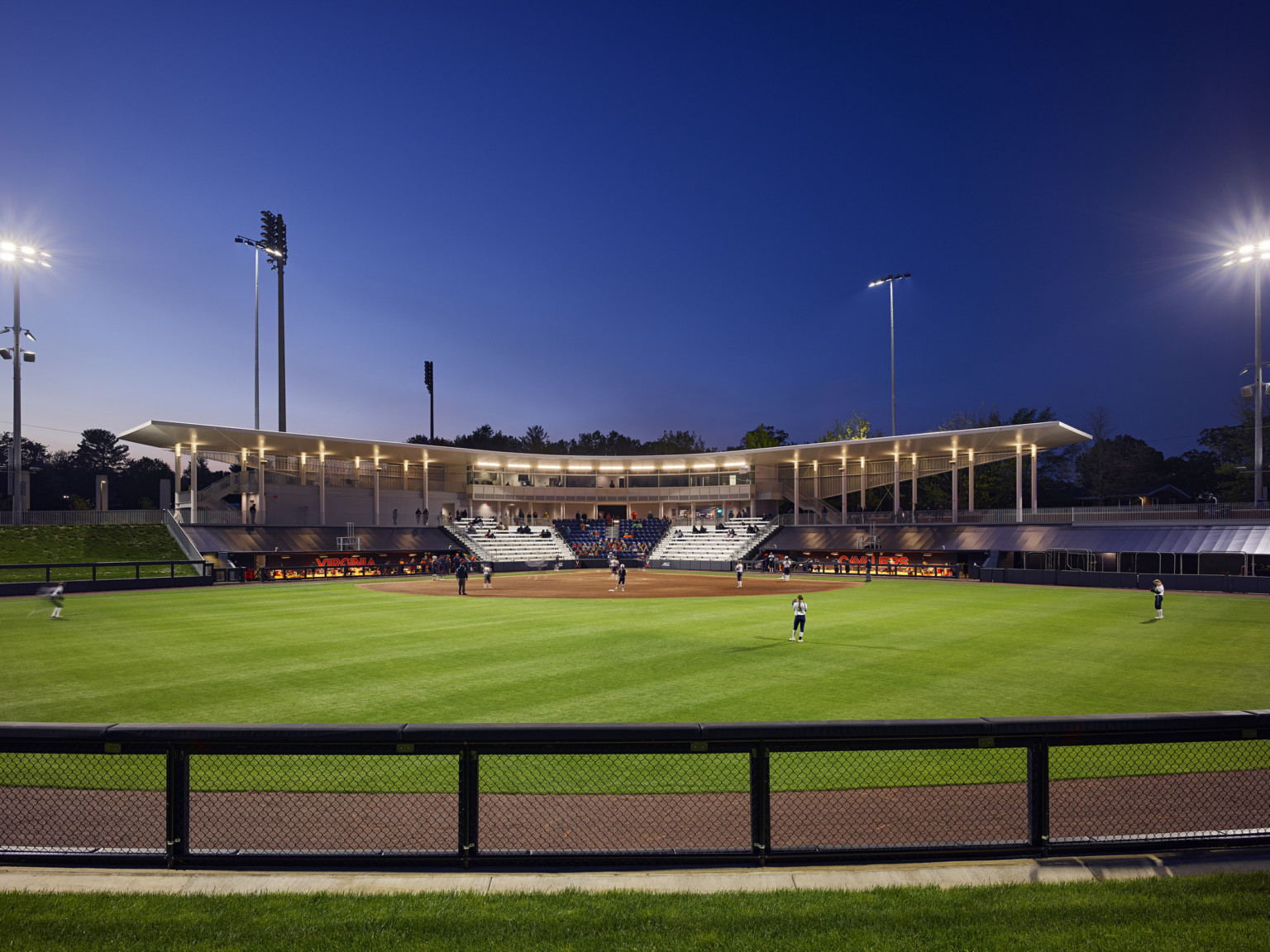 Baseball diamond seen from across the outfield from home plate. Canopy over press box behind blue, white seats; dugout fames