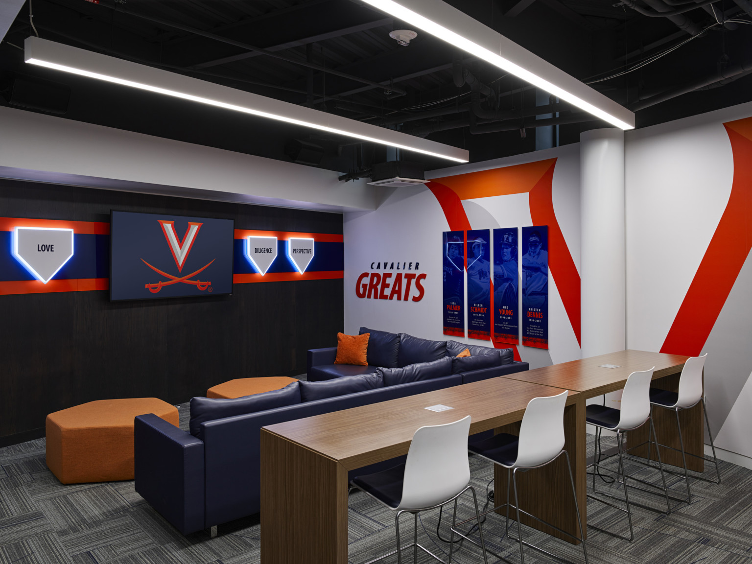 Players lounge with screen in front of mixed seating and tabletops. Mural, right, of Cavalier Greats. Illuminated values left