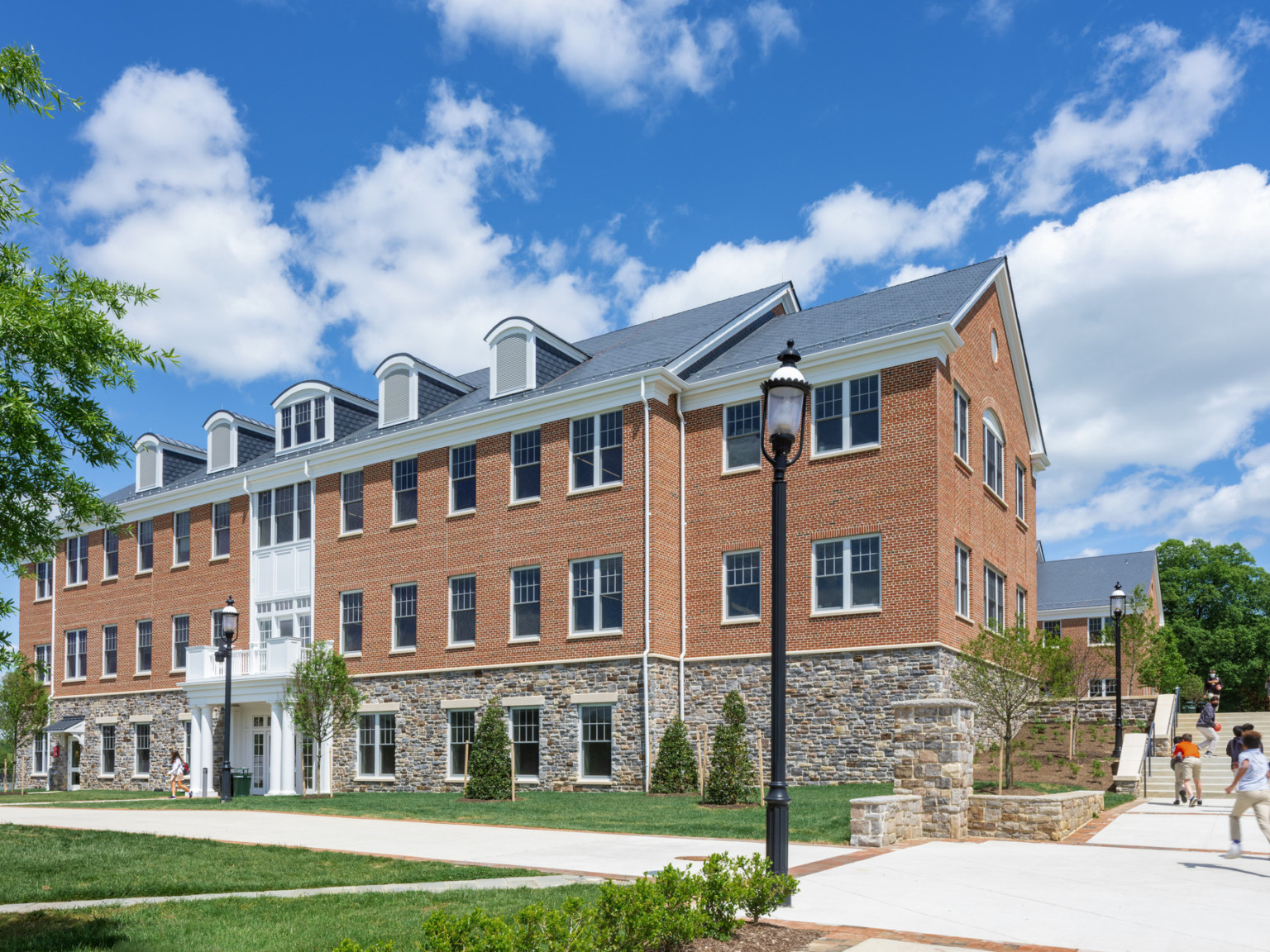 Side view of building with stone lower level built into hill with center covered entrance, stairs to right lead up the hill