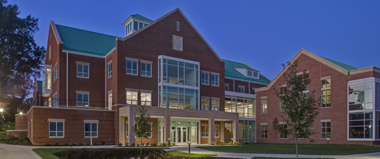 A multistory brick building with green roof and glass wall accents illuminated at night. Brown covered entry at driveway