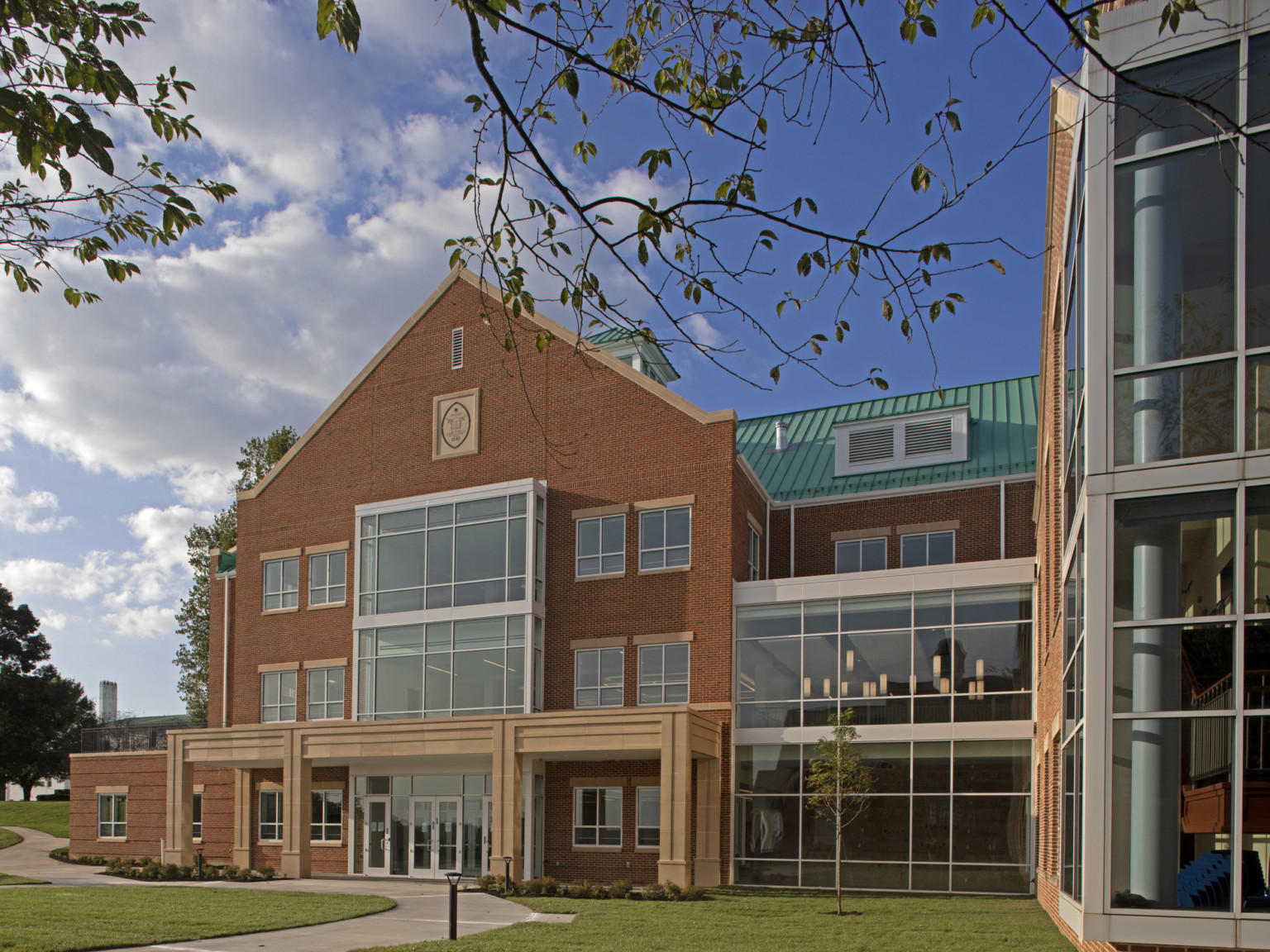 Glass double height additions from 3 story brick building with art deco carved stone canopy over entrance. Green roof