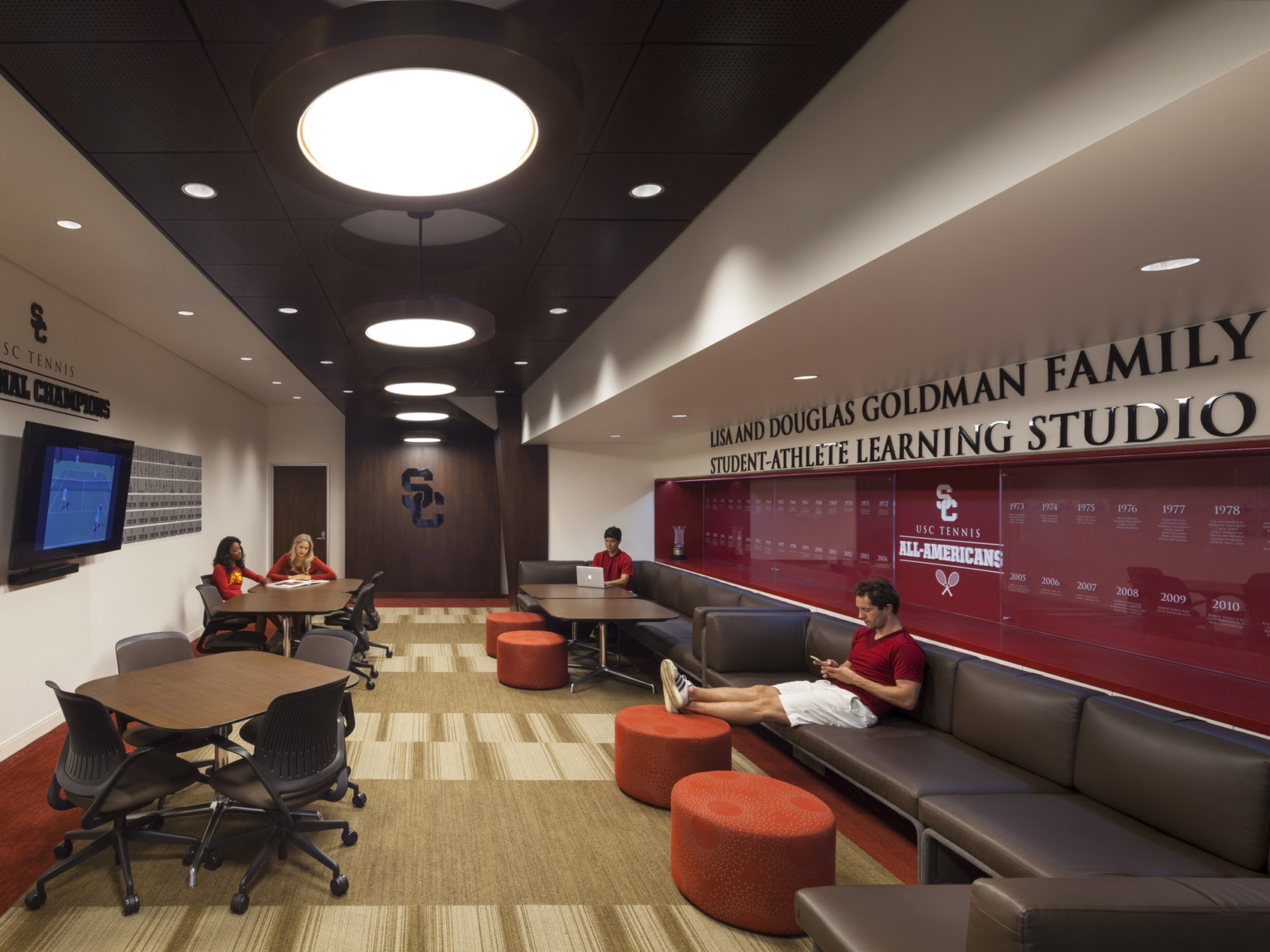 Long room labeled Learning Center. Flexible tables and chairs, brown couches line right wall below USC Tennis winning years