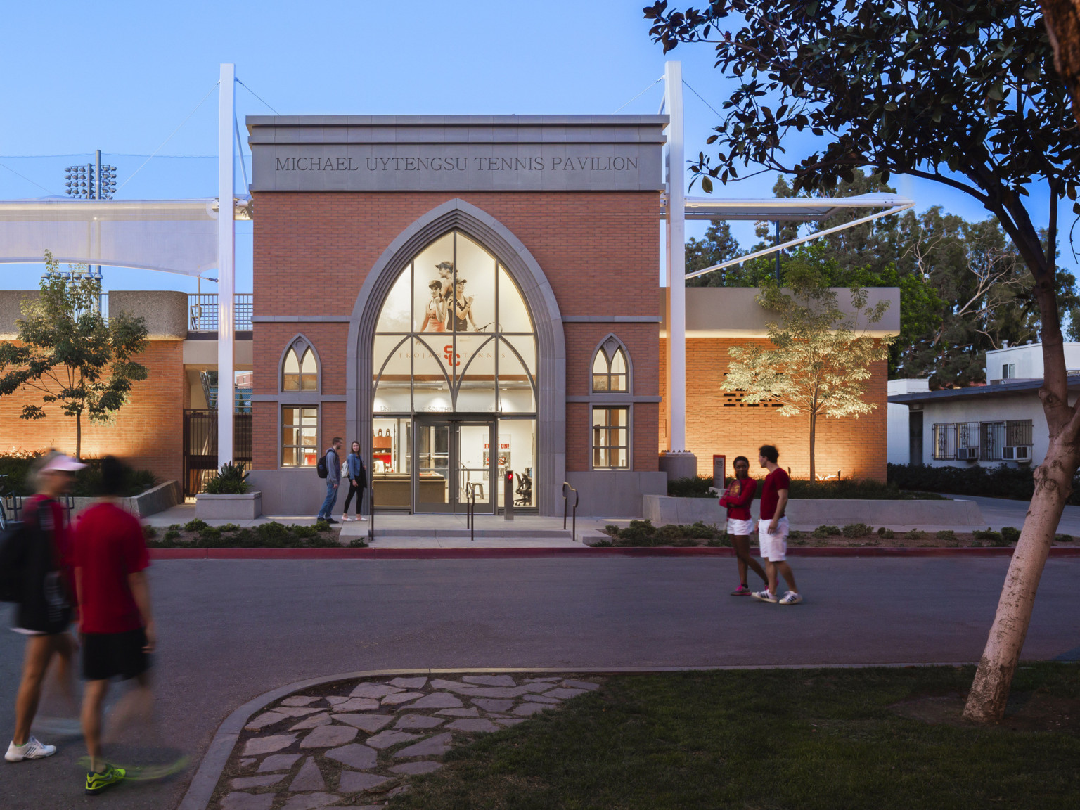 Double height brick building with Michael Uytengsu Tennis Pavilion carved over pointed arch lancelet windows and glass entry