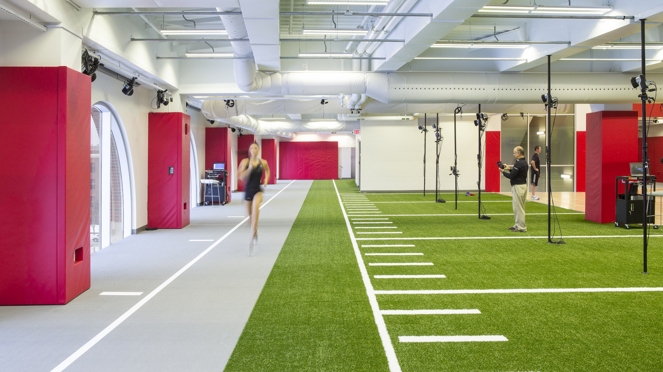 The University of Nebraska Athletic Performance Lab training facility with grey and turf floor in white room with red padding