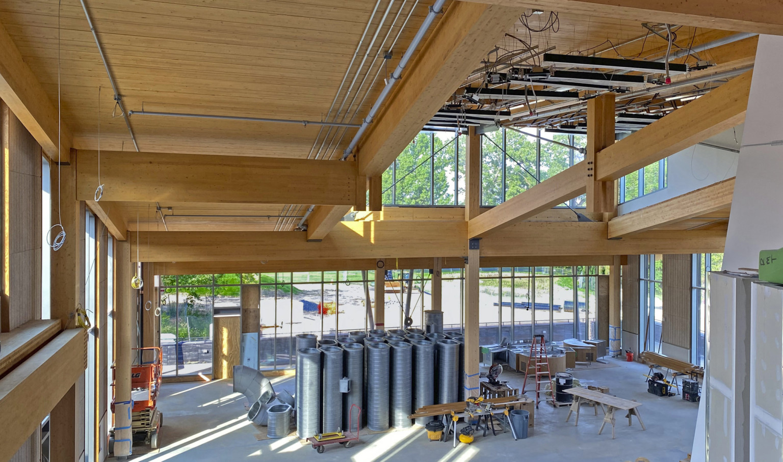 Dining commons interior under construction looking from upper level. Mass timber walls and ceiling, equipment and large windows