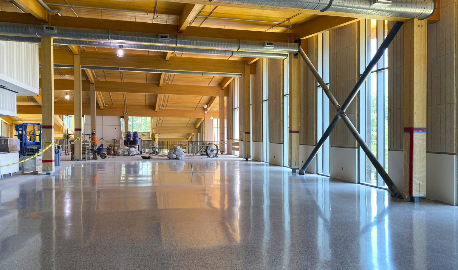 Dining commons interior under construction. Mass timber walls and ceiling exposed with ductwork and large windows