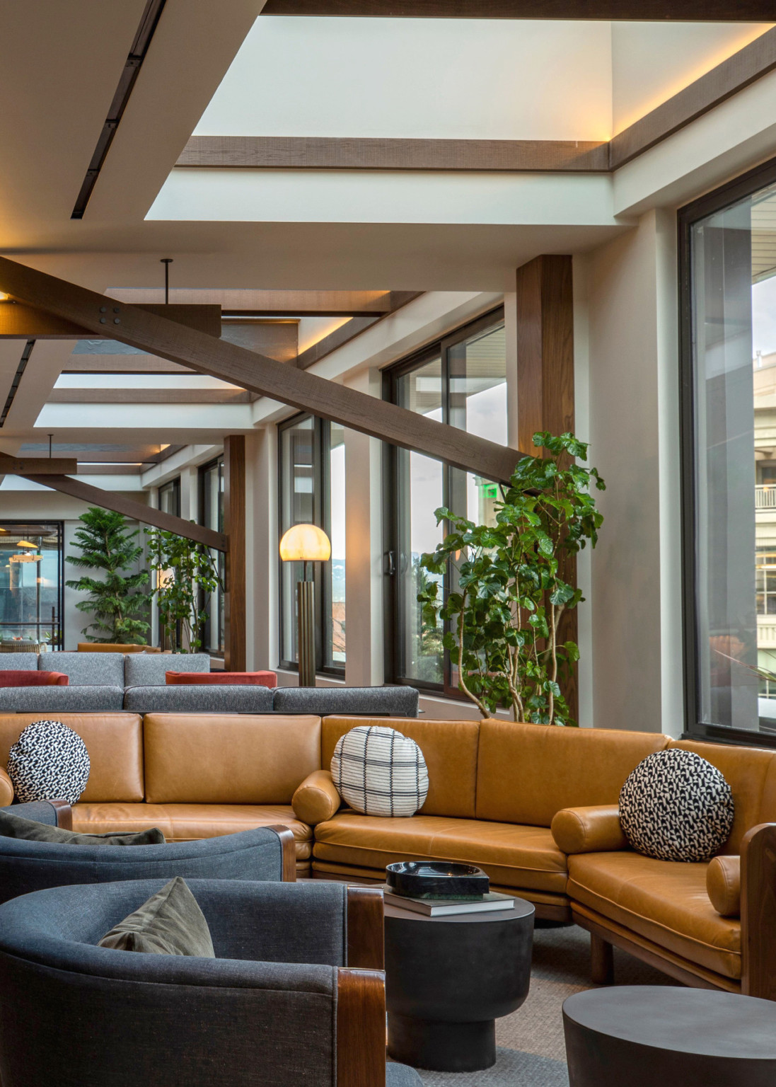 Upper level seating area with grey and brown couches along window lined wall with skylights above. Exposed wood trusses