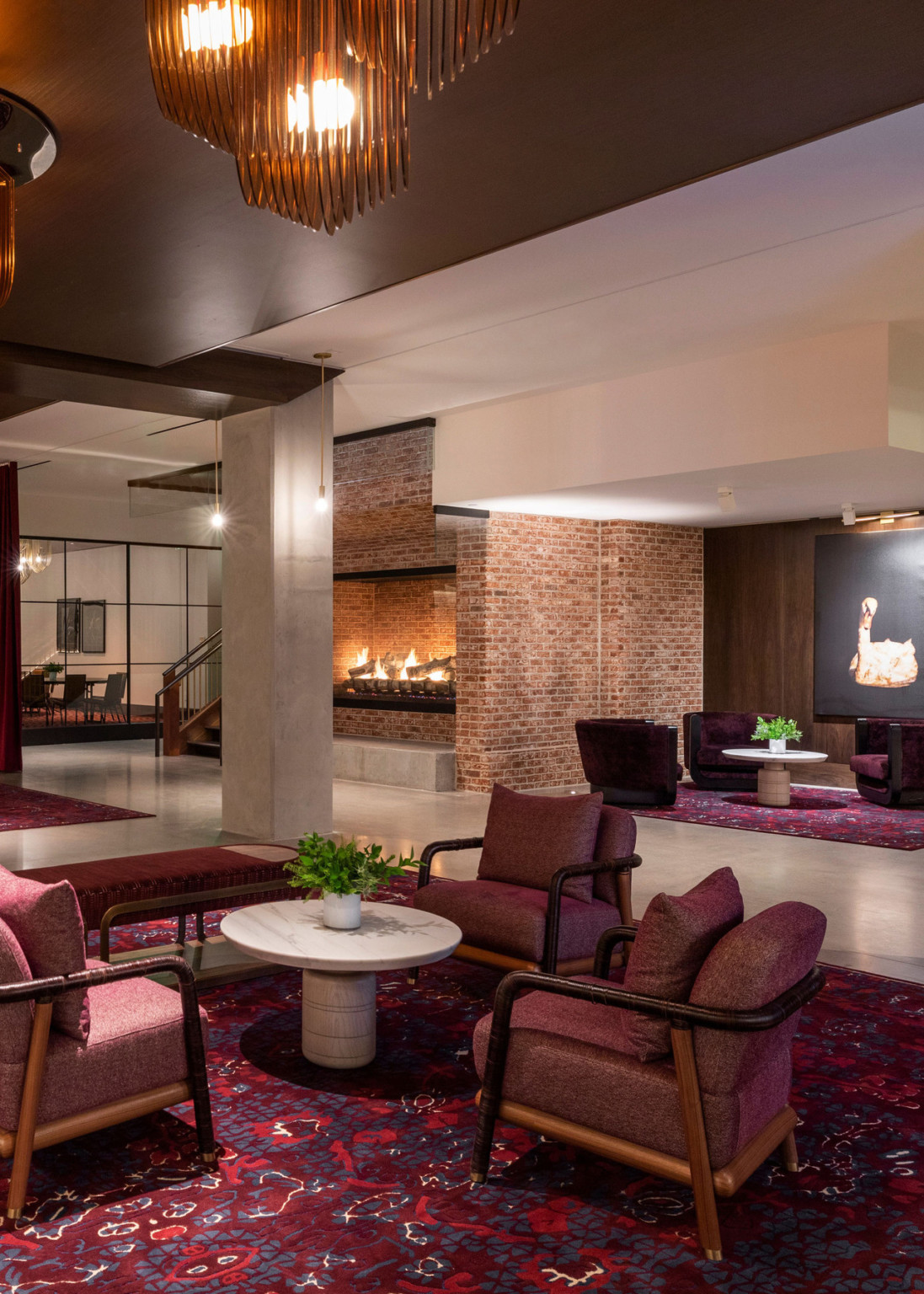 Interior seating with dark red carpet and arm chairs in exposed brick lobby with white columns and brown wood ceiling, chandeliers