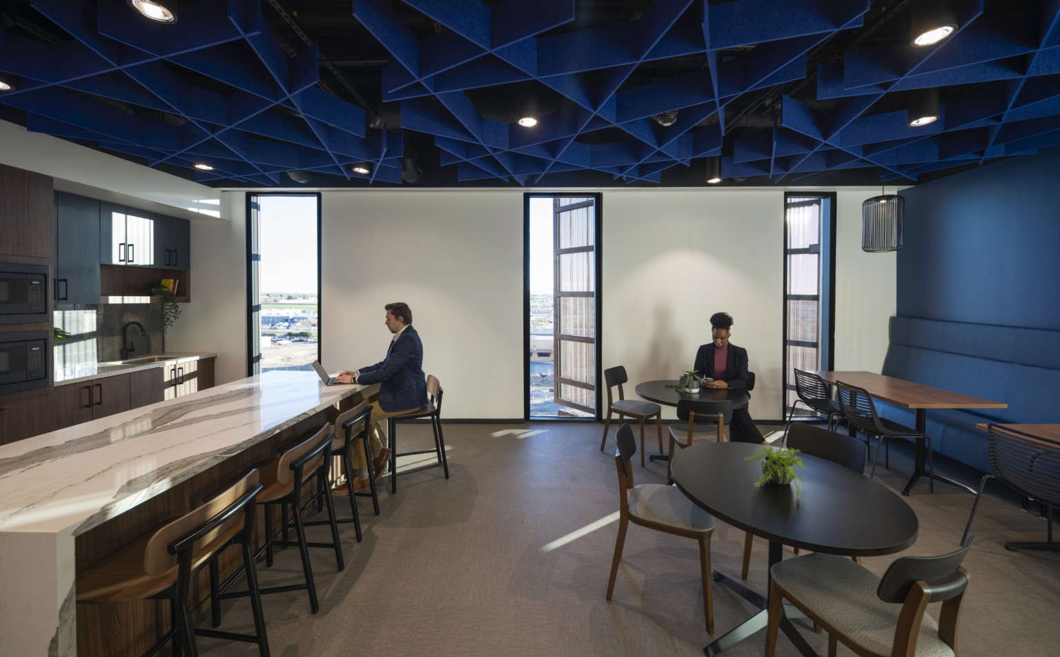 Office common space with blue accent wall and textural ceiling over mixed seating and marble counter, kitchenette left