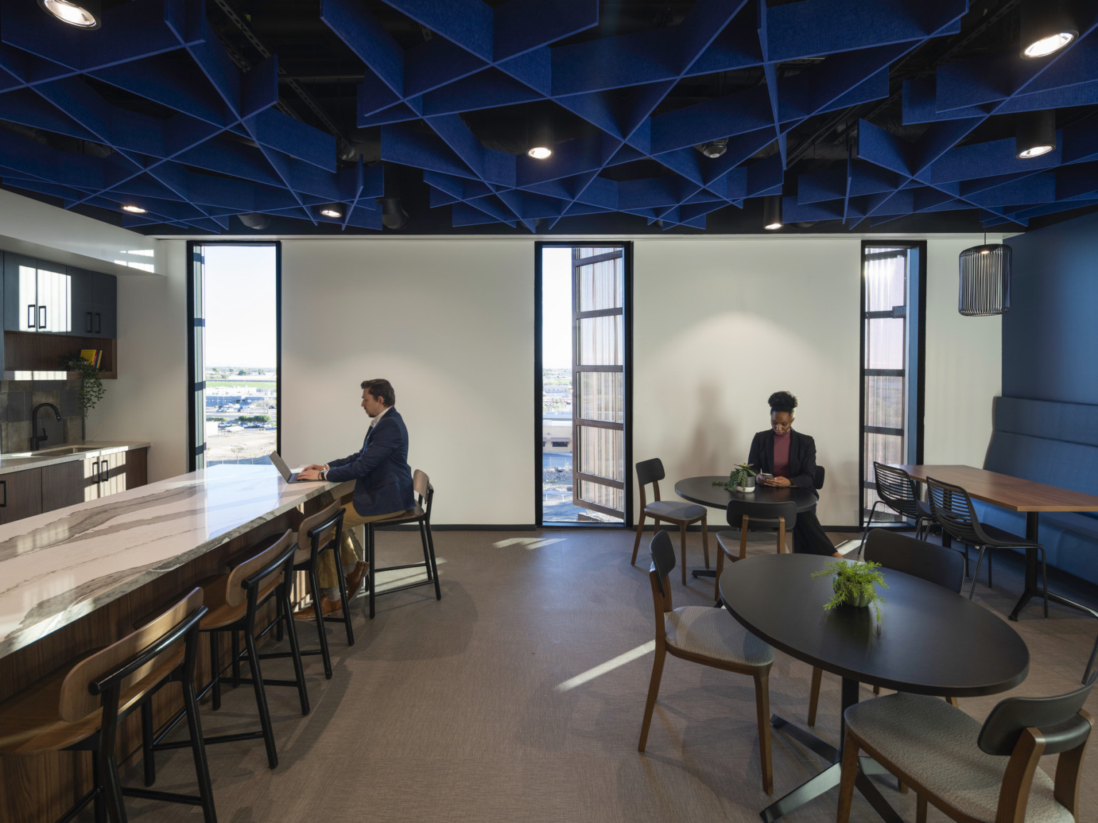 Office common space with blue accent wall and textural ceiling over mixed seating and marble counter, kitchenette left