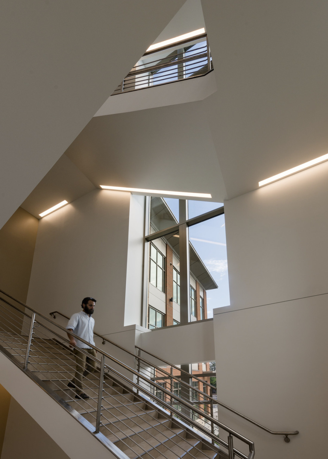 Multistory white open stairwell with light panels wrapping along edge of ceiling. Large windows run down back wall