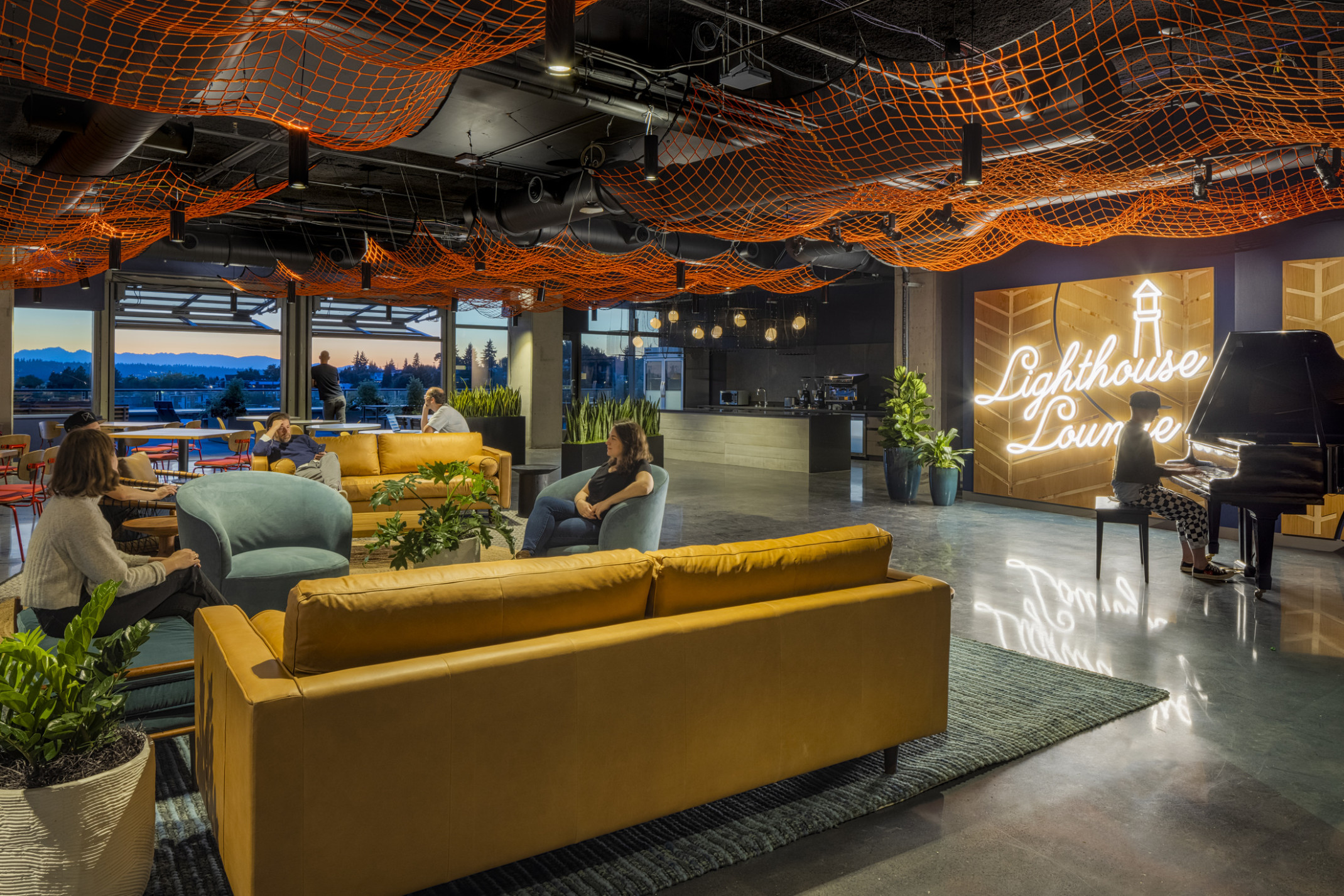 workplace lounge with piano and fishing net art installation, garage doors open to mountain views at sunset