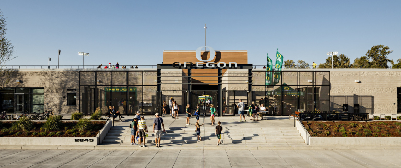 Papé Field entrance, 1 story concrete building with black gates and accents. Wood panels rise up at center with Oregon logo