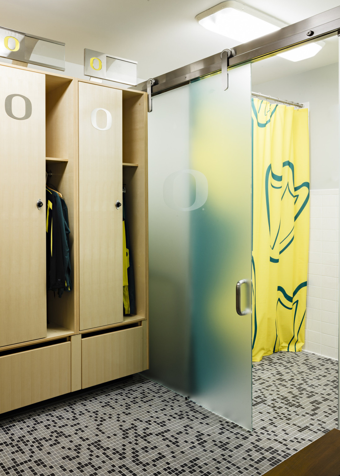 Lockers on tiled floor. Right, partially open foggy sliding glass door to shower with green and yellow curtain, white wall tile
