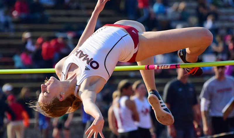 Woman in the middle of a high jump, bent over the yellow pole