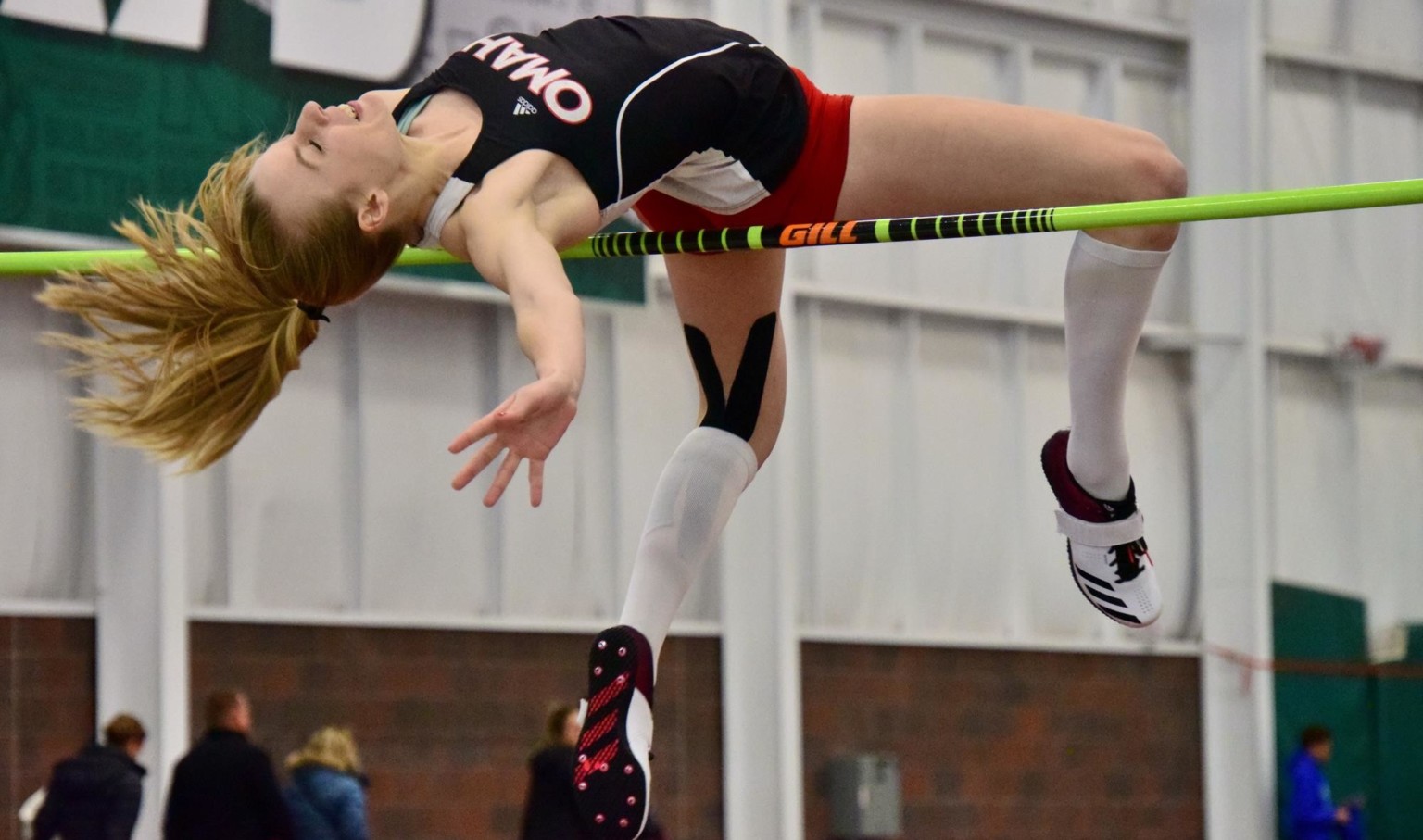 Woman in the middle of a high jump, bent over the yellow pole