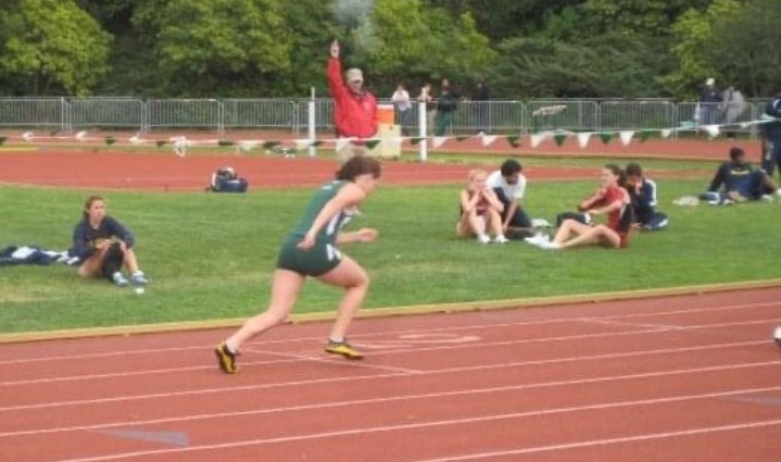 Woman running on brown round track with grassy center Woman running on brown round track with grassy center