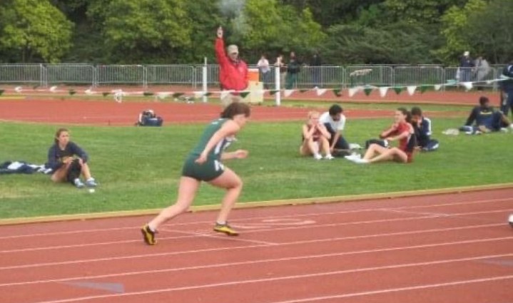 Woman running on brown round track with grassy center