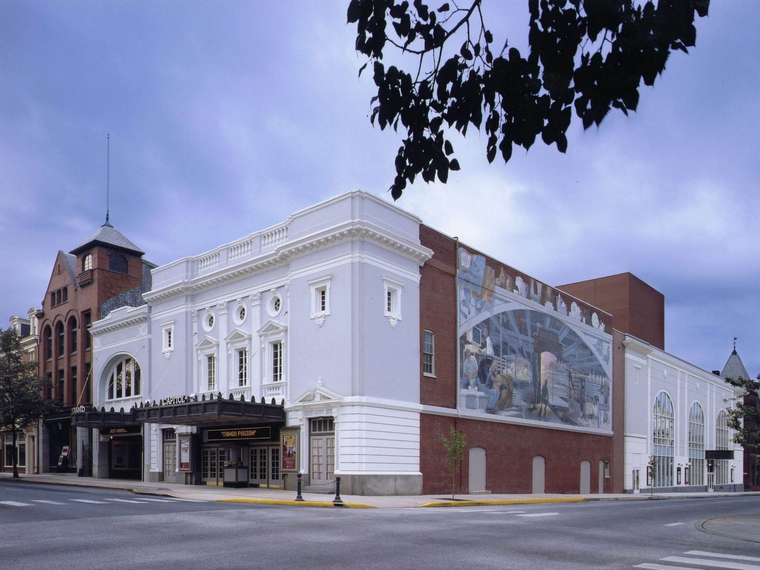 Exterior corner view of Capitol Theater with white front facade with moulding and black awning, mural on right brick wall