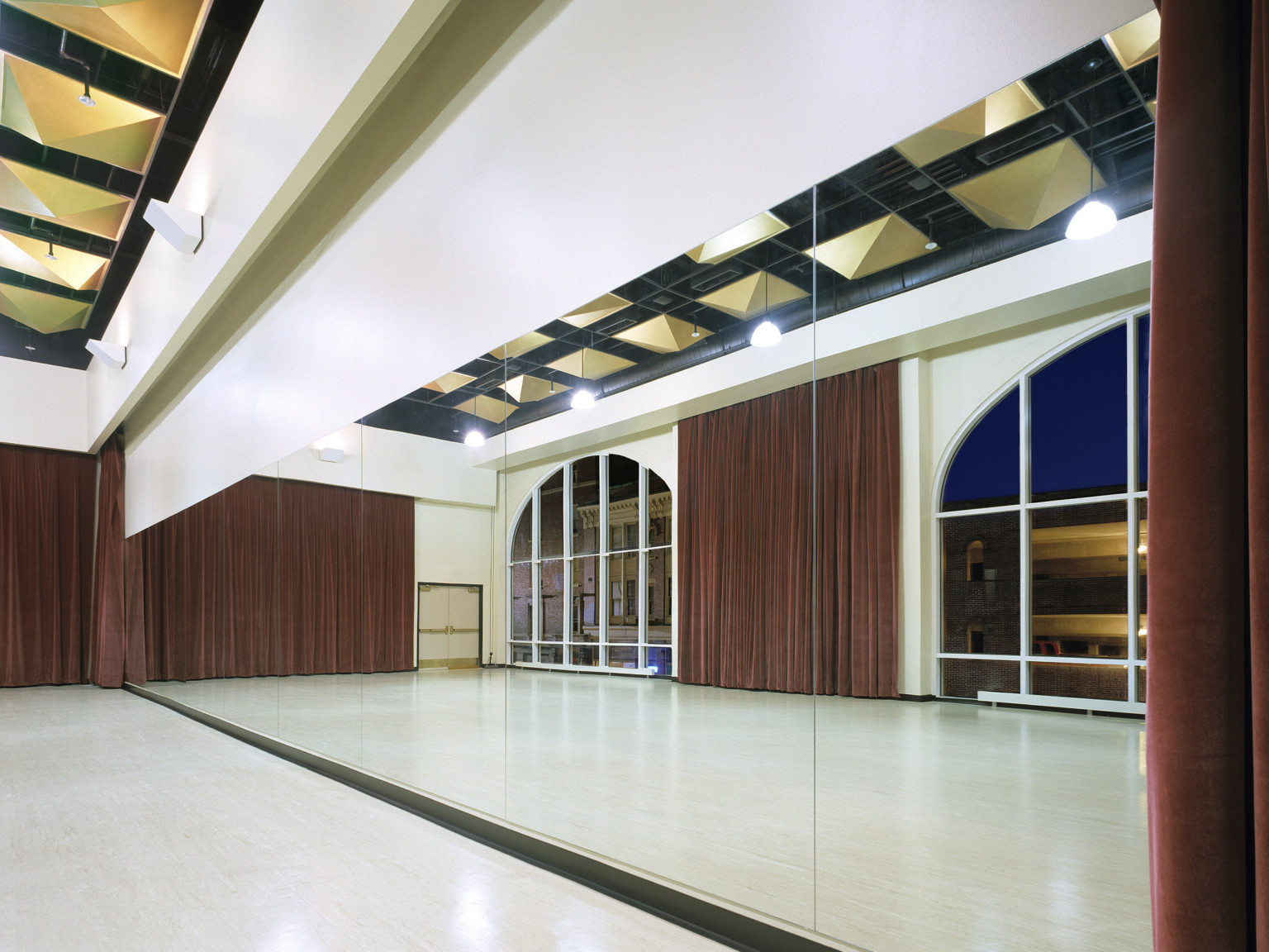 Reahearsal and gathering place with mirror wall reflecting arching floor to ceiling windows and dark red brown curtains