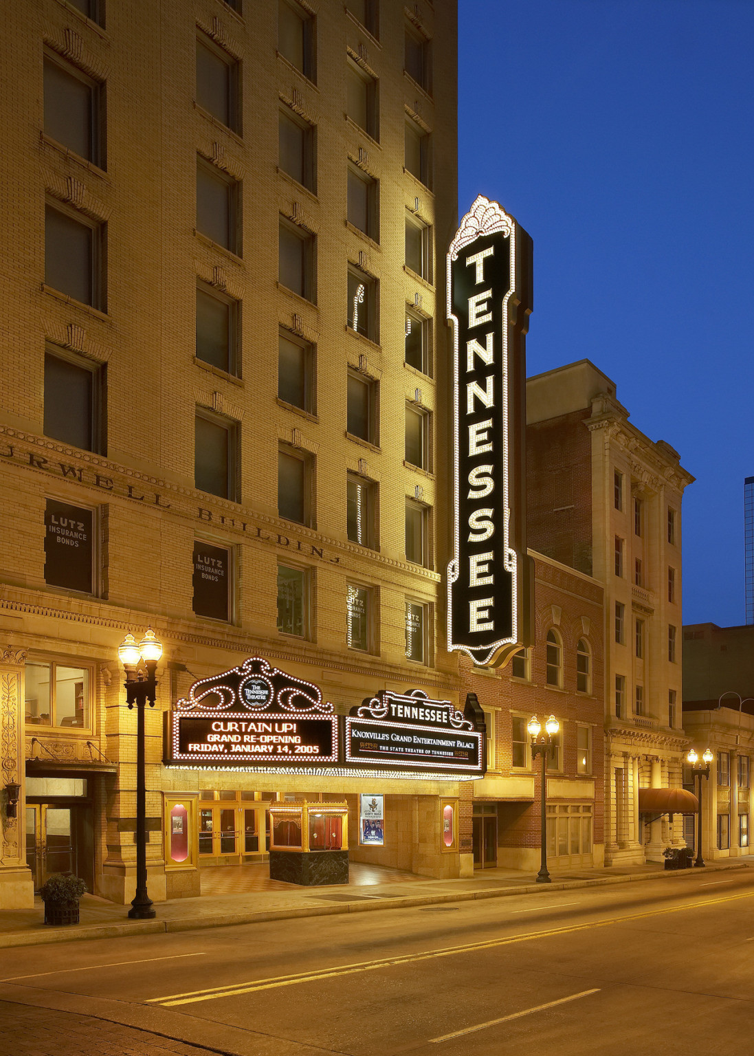 Blade sign reading Tennessee at front of theater hanging over marquee of multistory stone building, entry framed by streetlights