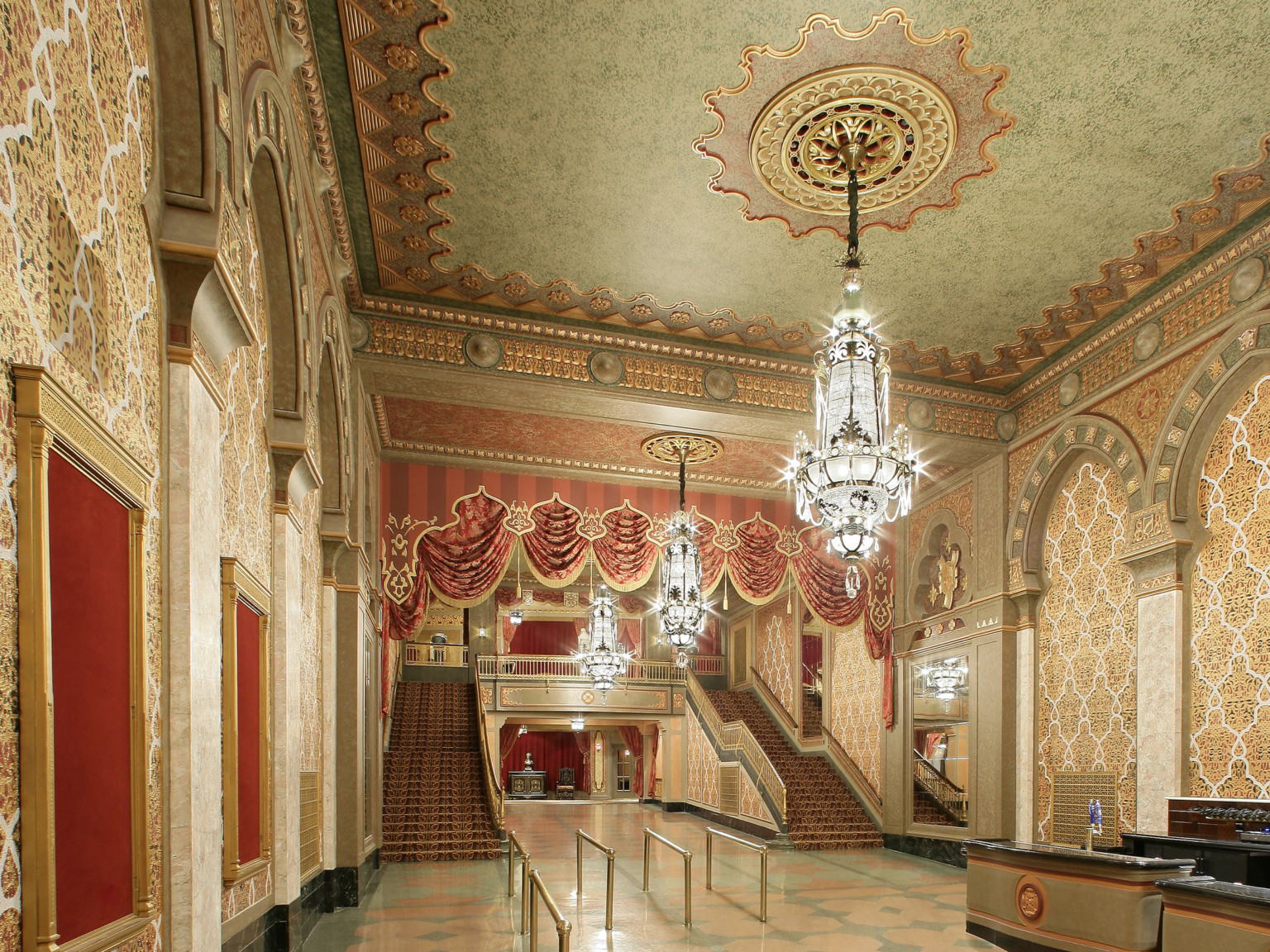 Double height lobby with large chandeliers framed by double staircase. Space divided by draped valance. Carvings on ceiling.