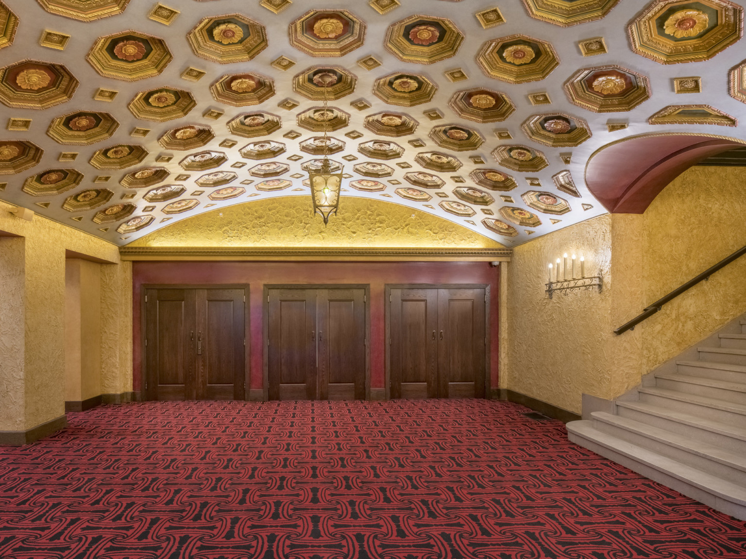 Hallway with arching ceiling and carved floral details in recessed octagonal niches. yellow stucco walls, red patterned carpet