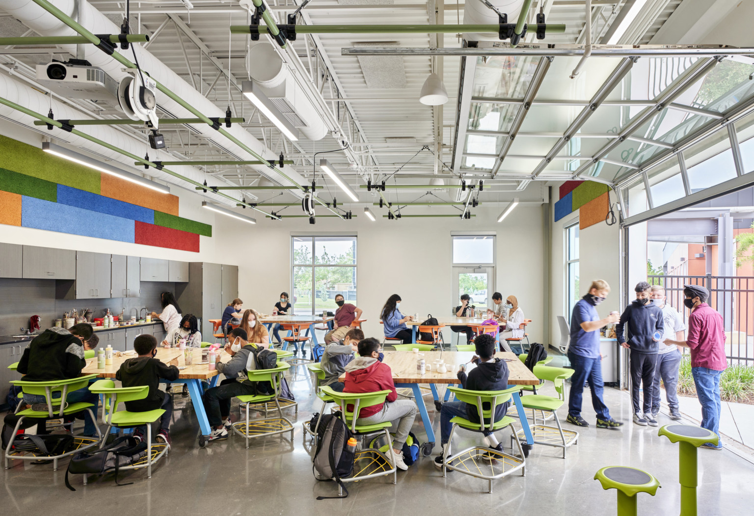 Flexible seating around tables in dining space. Garage door of windows opened to right. Green accents. Kitchenette left