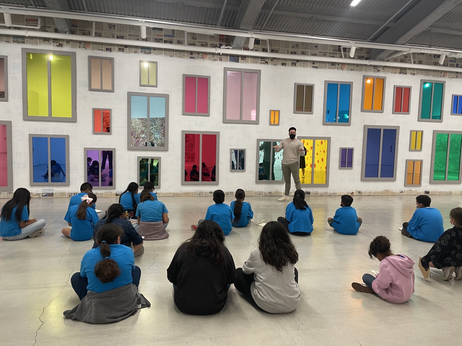students sitting on the floor looking at a wall of colorful windows at a museum